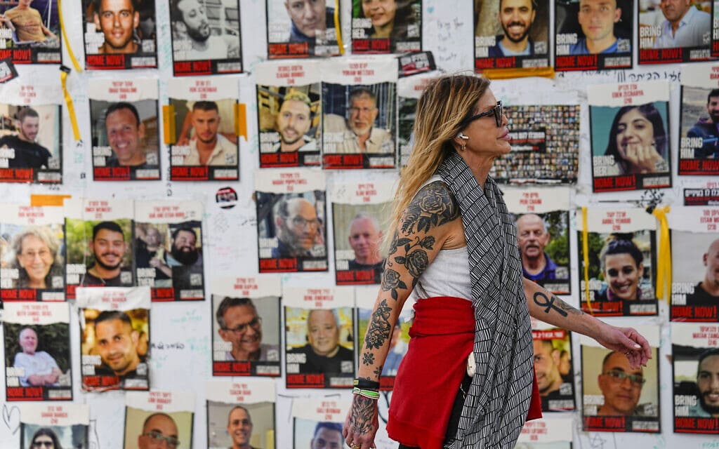 עוברת אורח חולפת בתל אביב על פני תמונות החטופים המוחזקים ברצועת עזה, 12 בפברואר 2024 (צילום: AP Photo/Ariel Schalit)