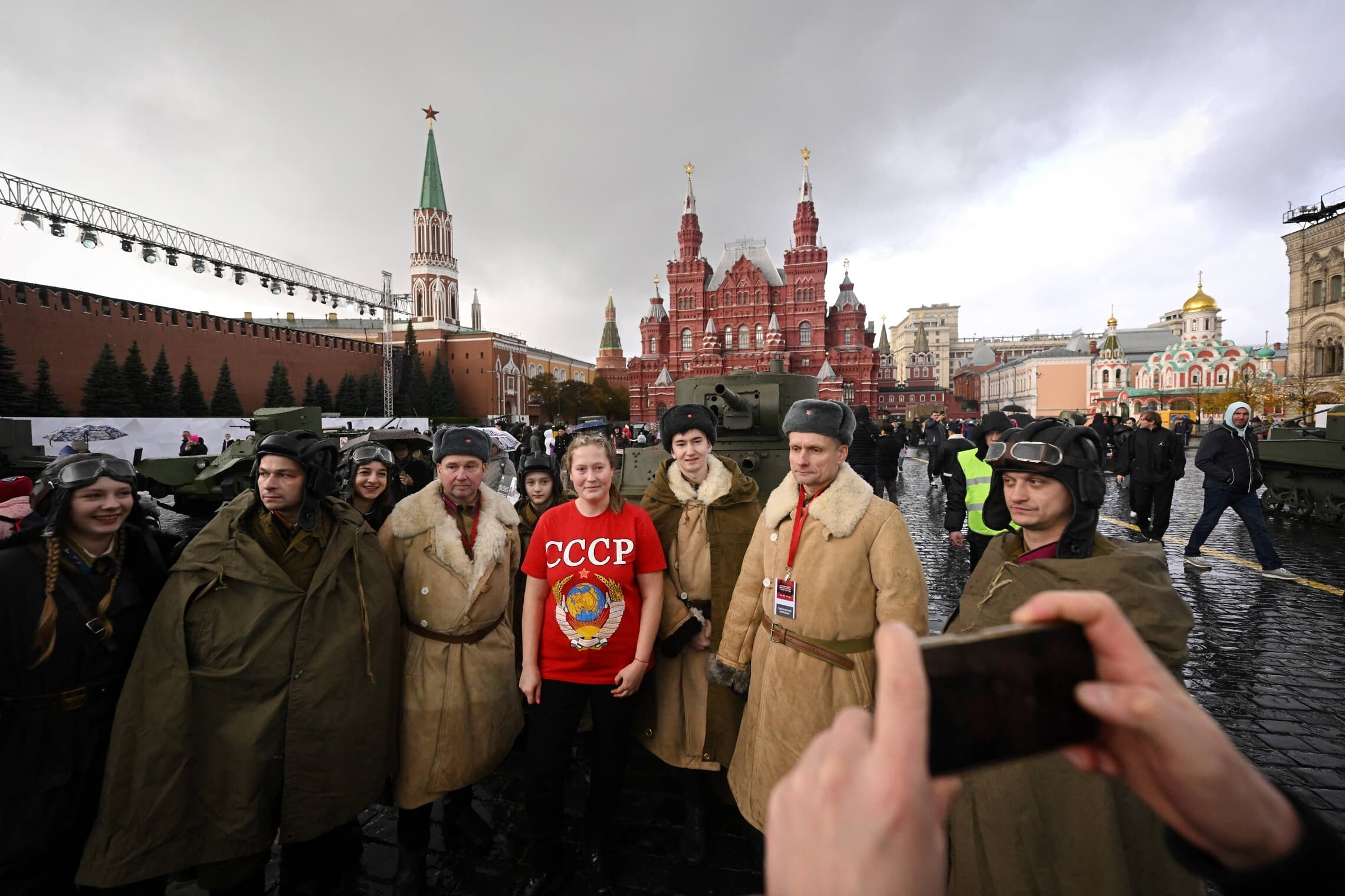 אישה רוסיה לבושה בחולצה עם לוגו של ברית המועצות מצולמת לצד חיילים מחופשים במדי מלחמת העולם השנייה בכיכר האדומה במוסקבה, 7 בנובמבר 2023 (צילום: Natalia KOLESNIKOVA / AFP)