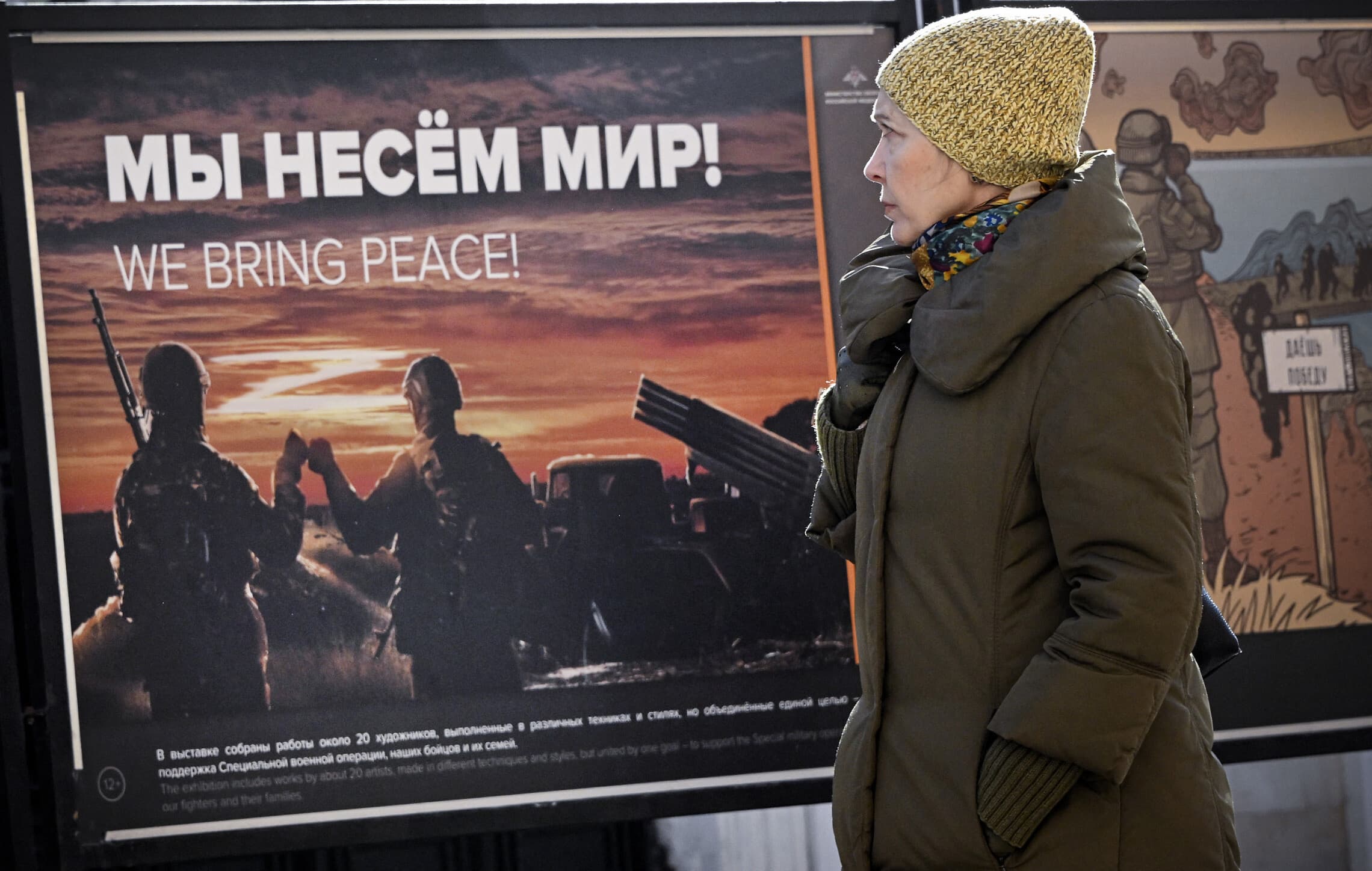 אישה מביטה בכרזה צבאית רוסית בתערוכה צבאית במוסקבה, 11 במרץ 2024 (צילום: Alexander NEMENOV / AFP)