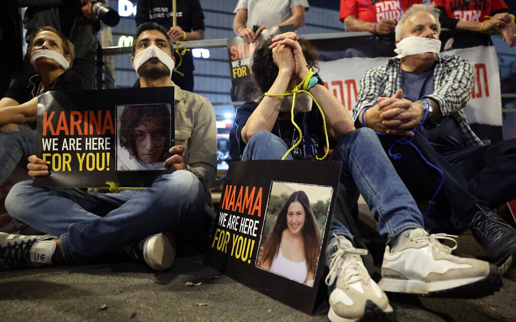 מוחים למען החטופים שקשרו את ידיהם וחסמו את פיהם בהפגנה בת"א, לצד תמונתן של החטופות נעמה לוי וקארינה ארייב ב-30 במרץ 2024 (צילום: Photo by JACK GUEZ / AFP)