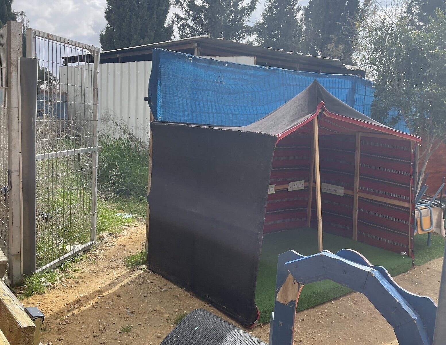 אוהל בדואי מיניאטורי למשחק ילדים בסמוך לצריף פח (הנגיש דרך שער פתוח) שמכיל גנרטור דיזל, במתחם גן הילדים בכפר אל-ערערה בנגב, 18 בפברואר 2024 (צילום: סו סורקס/ Times of Israel)