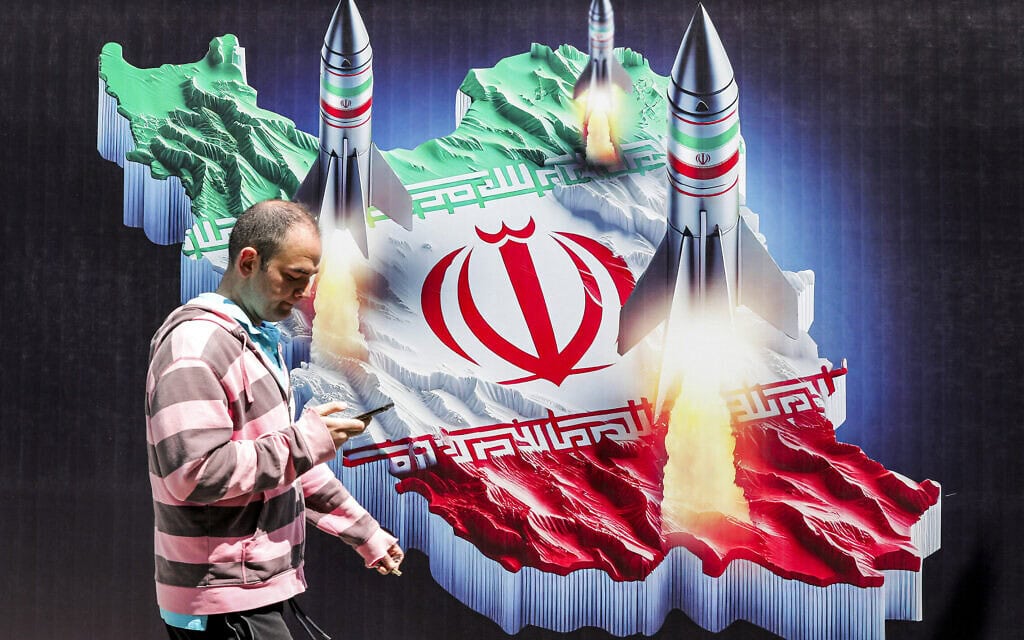 עובר אורח חולף בטהראן על פני שלט שבו נראים טילים משוגרים מאיראן, 15 באפריל 2024 (צילום: ATTA KENARE / AFP)