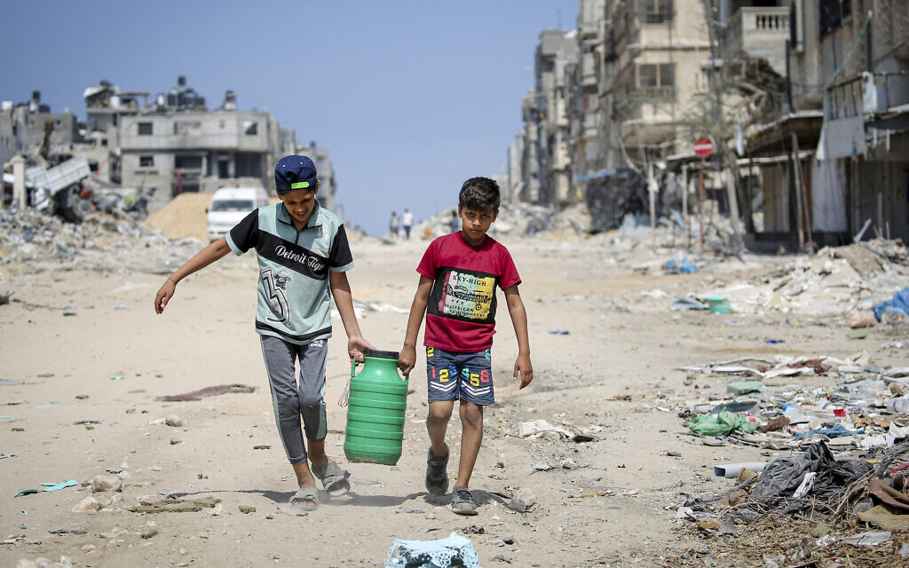 ילדים נושאים מים כשהם עוברים על פני מבנים שנהרסו במהלך ההפצצה הישראלית בחאן יונס, בדרום רצועת עזה ב-16 באפריל 2024 (צילום: AFP)