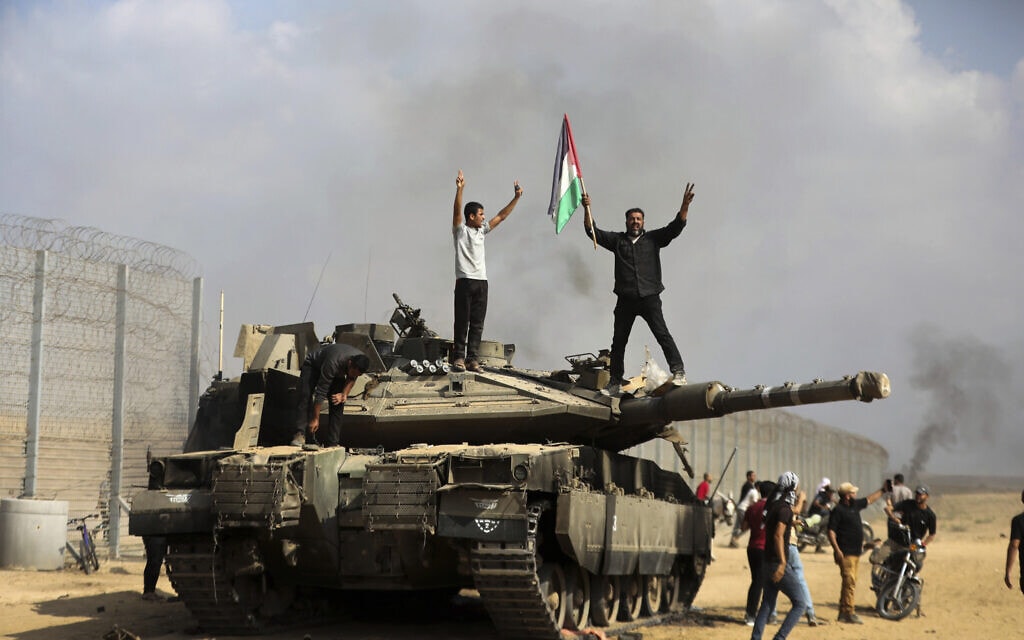 עזתים חוגגים על טנק ישראלי הרוס ליד גדר הגבול הפרוצה בין ישראל לעזה, ממזרח לחאן יונס, 7 באוקטובר 2023 (צילום: AP/Yousef Masoud)