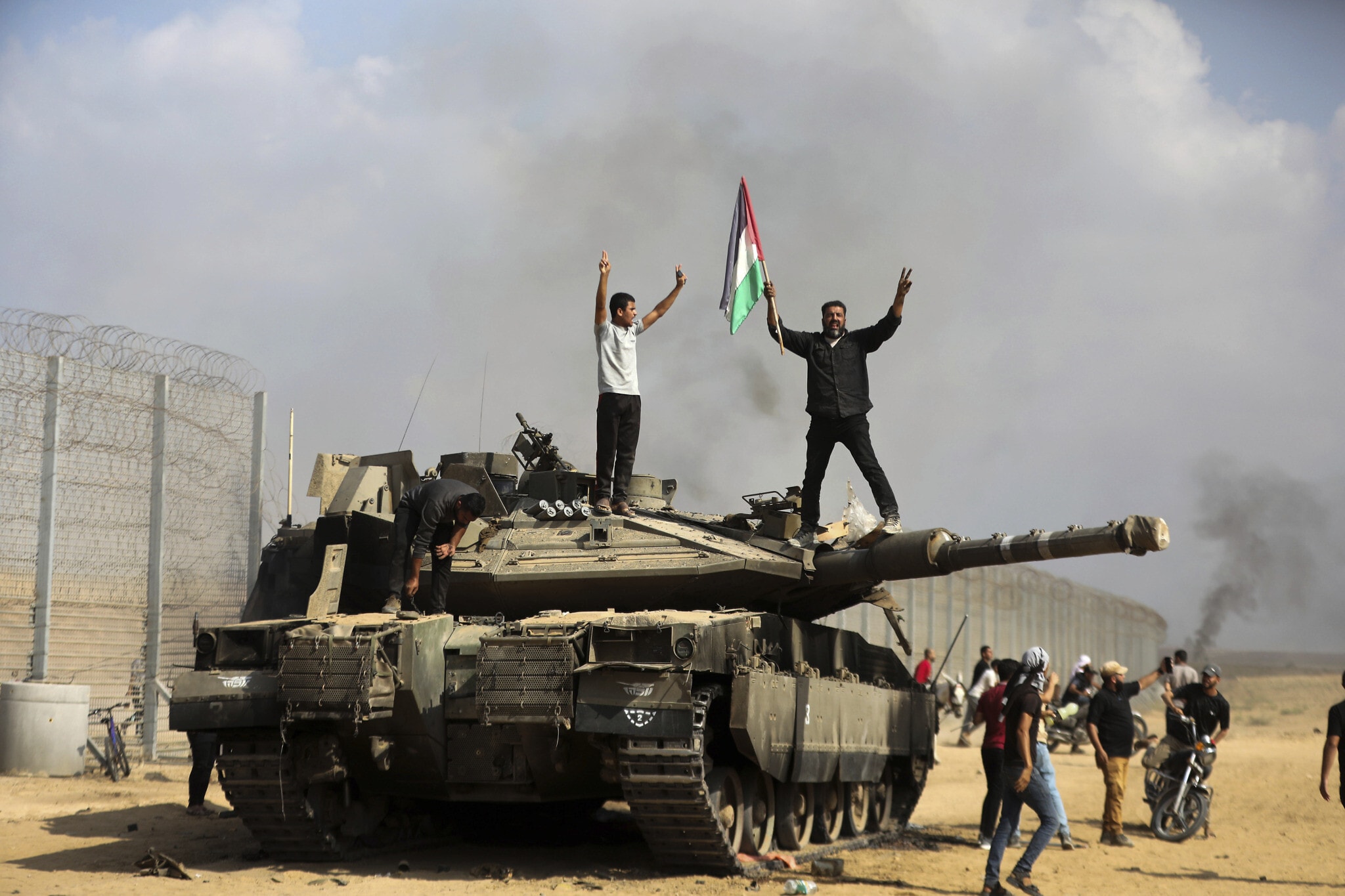 עזתים חוגגים על טנק ישראלי הרוס ליד גדר הגבול הפרוצה בין ישראל לעזה, ממזרח לחאן יונס, 7 באוקטובר 2023 (צילום: AP Photo/Yousef Masoud)