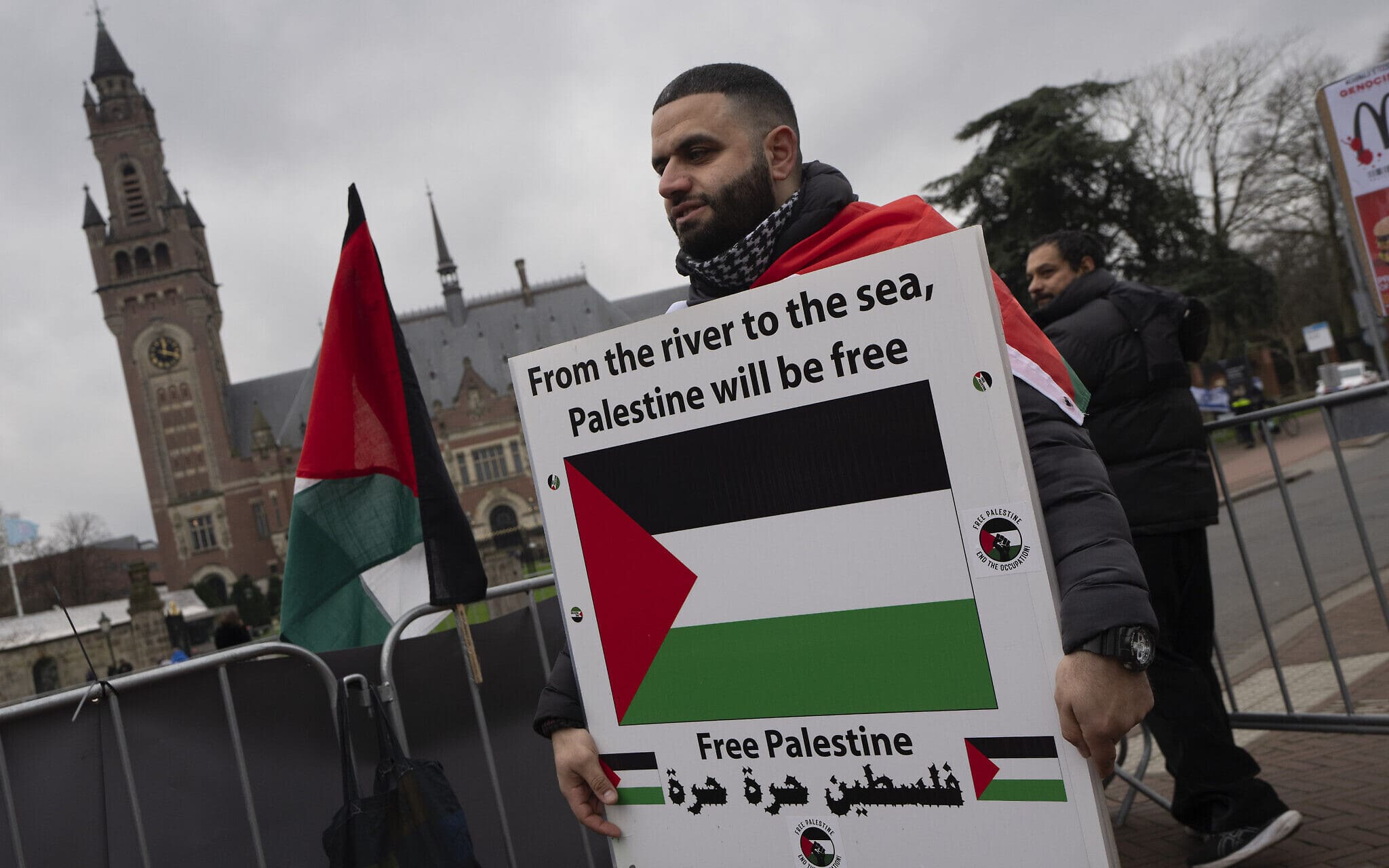 מפגין מחזיק שלט עם הכיתוב &quot;מהנהר ועד הים, פלסטין תהיה חופשית&quot; מחוץ לבית הדין הבינלאומי לצדק בהאג, הולנד, 21 בפברואר 2024 (צילום: AP Photo/Peter Dejong)