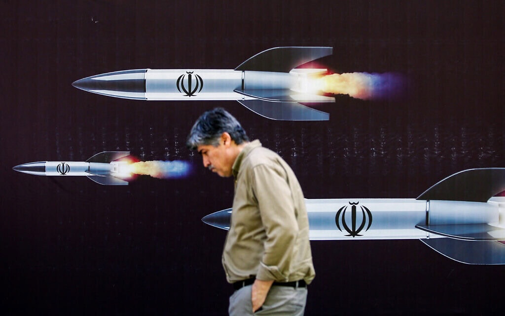 עובר אורח חולף בטהרן על פני שלט שבו נראים טילים משוגרים מאיראן, 19 באפריל 2024 (צילום: AFP)