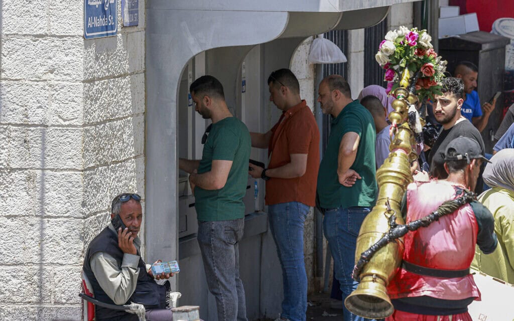 פלסטינים עומדים בתור למשיכת כסף מכספומט בשוק המרכזי ברמאללה, הגדה המערבית, 9 ביוני 2024 (צילום: Jaafar ASHTIYEH / AFP)