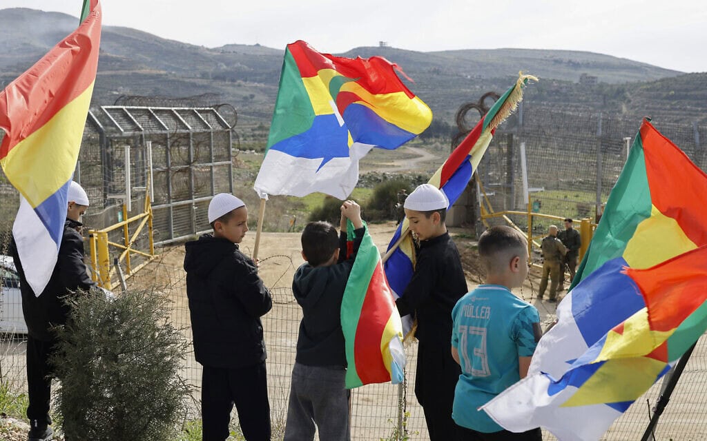 נערים דרוזים מחזיקים דגלים ליד חיילים ישראלים המאבטחים את גדר הגבול בכפר מג'דל שמס שברמת הגולן שבשליטת ישראל, בזמן שאנשים ממתינים להגעת משלחת מהצד הסורי של הגולן, ב-14 במרץ 2025 (צילום: John Wessels / AFP) נערים דרוזים מחזיקים דגלים ליד חיילים ישראלים המאבטחים את גדר הגבול בכפר מג'דל שמס שברמת הגולן שבשליטת ישראל, בזמן שאנשים ממתינים להגעת משלחת מהצד הסורי של הגולן, ב-14 במרץ 2025 (צילום: John Wessels / AFP)