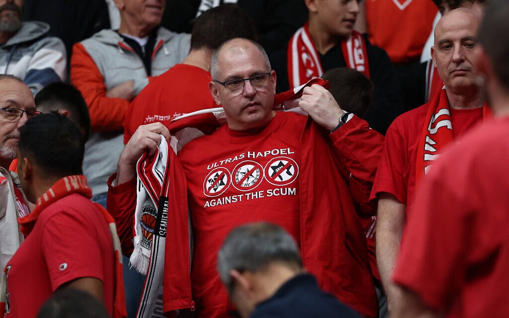 אוהד הפועל תל אביב לובש את החולצה שהמשטרה אסרה על לבישתה במגרשי הכדורגל ב-16 בדצמבר 2025, במשחק כדורסל בין הפועל תל אביב והכוכב האדום בלגרד במסגרת טורניר היורוליג (צילום: דני מרון/פלאש90) אוהד הפועל תל אביב לובש את החולצה שהמשטרה אסרה על לבישתה במגרשי הכדורגל ב-16 בדצמבר 2025, במשחק כדורסל בין הפועל תל אביב והכוכב האדום בלגרד במסגרת טורניר היורוליג (צילום: דני מרון/פלאש90)