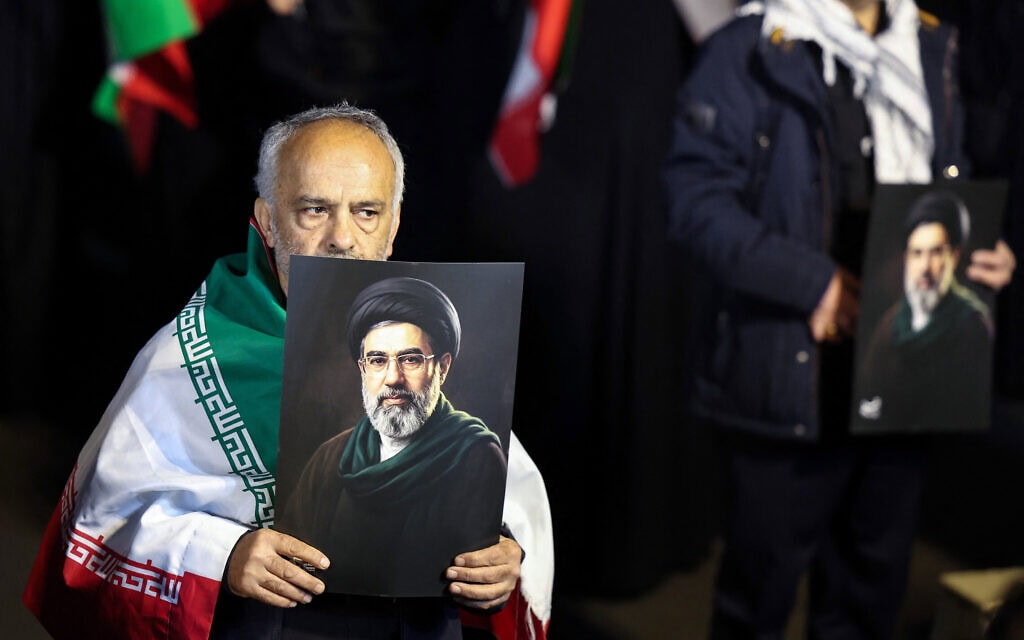 אדם עטוף בדגל איראן מחזיק בתמונה של מוג'תבא חמינאי במהלך עצרת תמיכה במשטר האיראני בטהרן, 25 במרץ 2026 (צילום: AFP) אדם עטוף בדגל איראן מחזיק בתמונה של מוג'תבא חמינאי במהלך עצרת תמיכה במשטר האיראני בטהרן, 25 במרץ 2026 (צילום: AFP)