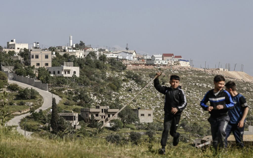 ילדים משחקים ליד הכפר ג'אלוד, מדרום לשכם שבגדה המערבית, כשברקע נראית ההתנחלות אחיה, 19 באפריל 2026 (צילום: Zain JAAFAR / AFP)