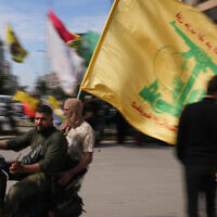 גברים רוכבים על קטנוע ומניפים דגל של חזבאללה בדאחייה, ביירות, לבנון, 25 באפריל 2026