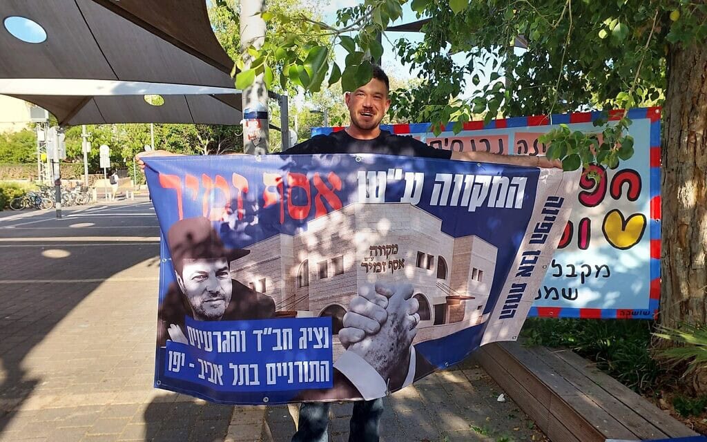 עומר נחמני מציג כרזה עם הכיתוב: "המקווה על שם אסף זמיר", 28 במאי 2026 (צילום: עומר שרביט) עומר נחמני מציג כרזה עם הכיתוב: "המקווה על שם אסף זמיר", 28 במאי 2026 (צילום: עומר שרביט)