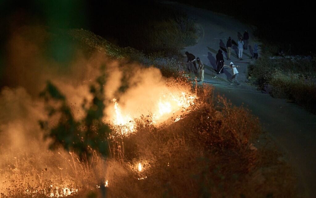 מתנחלים ישראלים מיידים אבנים ברוגטקות, בזמן שצמחייה בוערת בשולי הדרך לאחר שפלסטינים הציתו אותה כדי למנוע מהם להתקרב לכפר סנג'יל שבגדה המערבית. 17 ביולי 2026 (צילום: AP Photo/Leo Correa) מתנחלים ישראלים מיידים אבנים ברוגטקות, בזמן שצמחייה בוערת בשולי הדרך לאחר שפלסטינים הציתו אותה כדי למנוע מהם להתקרב לכפר סנג'יל שבגדה המערבית. 17 ביולי 2026 (צילום: AP Photo/Leo Correa)