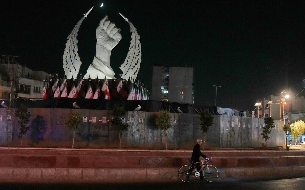 גבר נושא את אופניו מול אנדרטה המציגה את אגרופו הקמוץ של מנהיגה העליון המנוח של איראן, איאתוללה עלי חמינאי, שנהרג בתקיפה האמריקאית-ישראלית ב-28 בפברואר, בכיכר המהפכה האסלאמית בטהרן. 19 ביולי 2026 (צילום: AP Photo/Vahid Salemi)