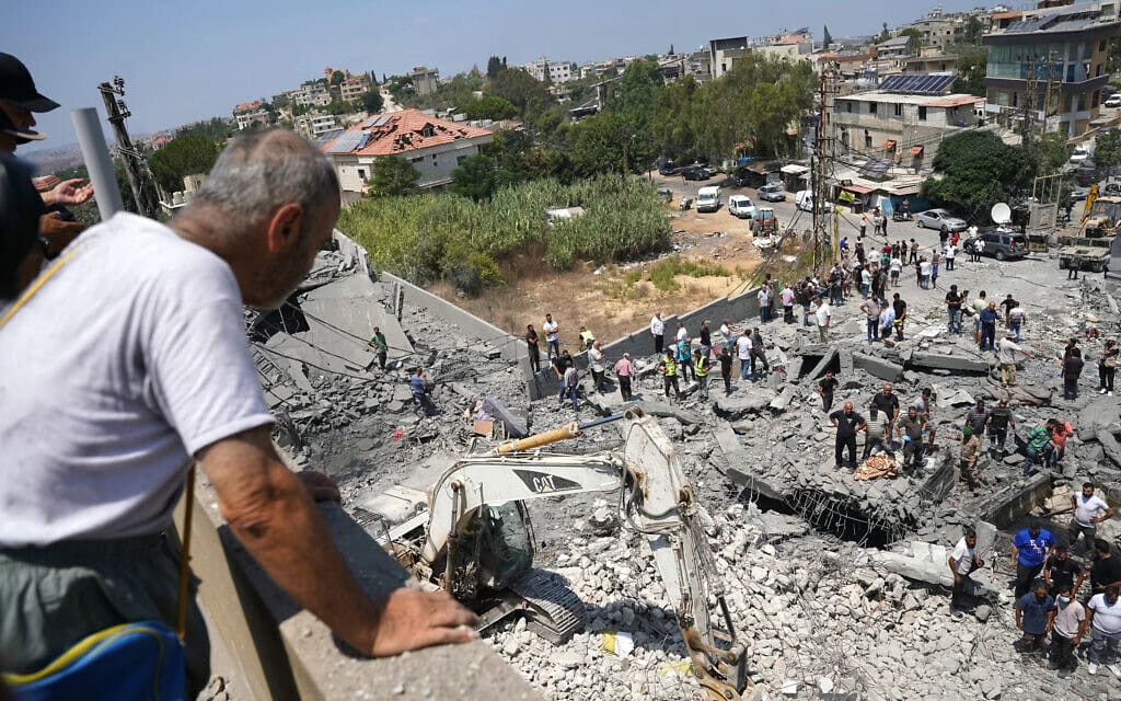 גבר מביט בצוותי עזרה ראשונה, תושבים וכלים כבדים המחפשים בזירת תקיפה אווירית ישראלית שכוונה לשכונה בכפר דיר א-זהראני שבדרום לבנון. 15 באוגוסט 2026 (צילום: Abbas FAKIH / AFP)