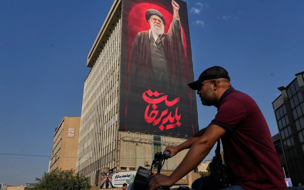 גבר רוכב על אופנוע וחולף על פני שלט חוצות הנושא את הכיתוב בפרסית: "עלינו לקום" ותמונה של מנהיגה העליון המנוח של איראן, האייתוללה עלי חמינאי, 15 באוגוסט 2026 (צילום: AP Photo/Vahid Salemi)